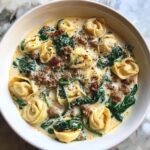Close-up of a hearty bowl of creamy tortellini soup featuring cheese tortellini, ground sausage, and wilted spinach.