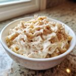 A white bowl filled with creamy shredded chicken, likely made using homemade cream of chicken soup, topped with red pepper flakes.