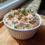 A close-up of creamy smoked salmon dip garnished with fresh dill and paprika in a white bowl.