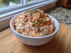 A white bowl filled with creamy smoked salmon dip, garnished generously with fresh dill and paprika.