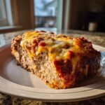 A thick slice of moist crockpot French onion meatloaf topped with melted, bubbly cheese, served on a white plate.