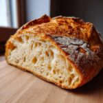 Close-up of a freshly baked italian bread loaf cut in half, showing an open, airy crumb and a deeply golden, crusty exterior.