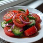Close-up of a fresh cucumber tomato salad featuring sliced tomatoes, cucumbers, and red onion tossed in a light dressing.