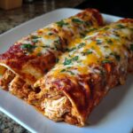 Close-up of two easy chicken enchiladas covered in red sauce, melted cheddar and Monterey Jack cheese, and fresh parsley.