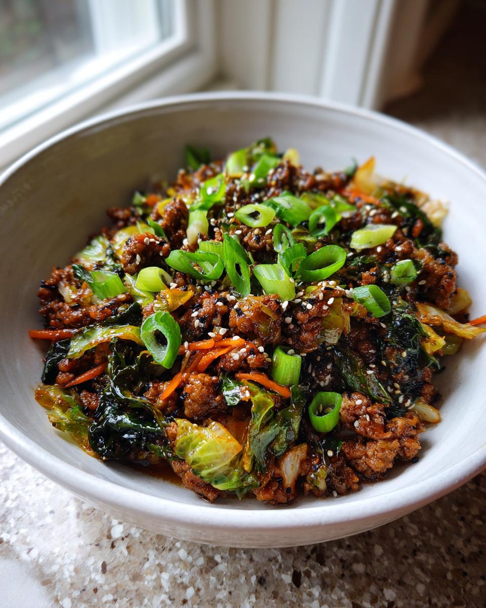 Close-up of a savory egg roll in a bowl mixture with ground meat, cabbage, carrots, topped with sliced green onions and sesame seeds.