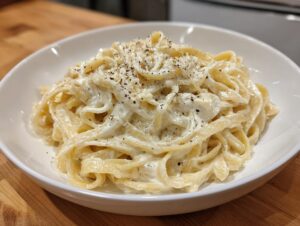 A white bowl filled with fettuccine pasta coated in rich, creamy olive garden alfredo sauce and topped with fresh black pepper.
