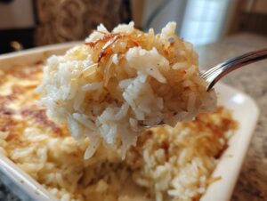 Close-up of a fork lifting a serving of creamy french onion butter rice topped with golden caramelized onions.