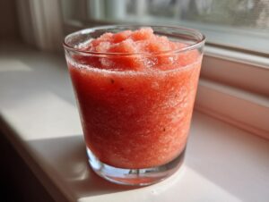 A bright red, icy strawberry daiquiri served in a clear glass sitting on a sunny windowsill.