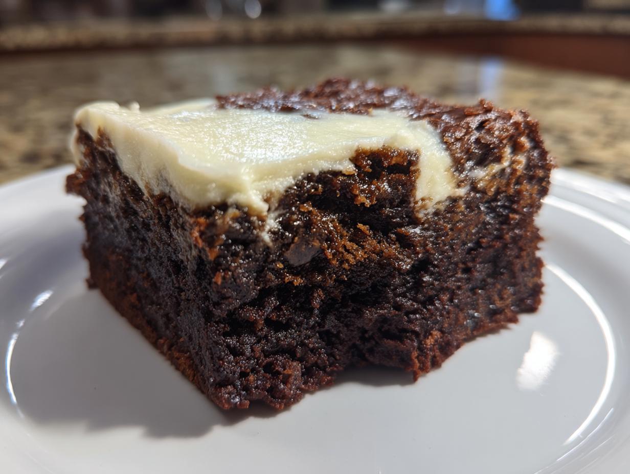 Close-up of a rich, dark gingerbread brownies slice topped with a swirl of white cream cheese frosting.