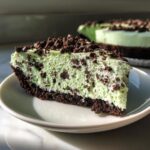 A close-up slice of creamy, light green grasshopper pie with a dark chocolate crust and chocolate chip topping.