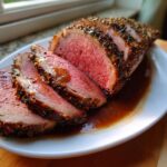 Slices of a perfectly cooked, medium-rare rib roast with a dark herb crust, resting in rich brown au jus.