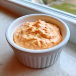 Creamy, orange-hued homemade big mac sauce speckled with red spices, served in a small white dipping bowl.