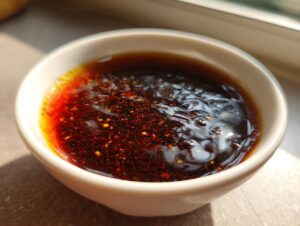 Close-up of rich, dark homemade teriyaki sauce with visible spices and oil separation in a small white bowl.