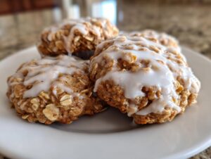 Four delicious iced oatmeal cookies piled on a white plate, featuring visible oats and thick white icing.