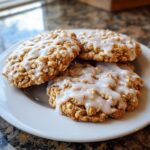 Close-up of three textured iced oatmeal cookies drizzled with white vanilla glaze on a white plate.