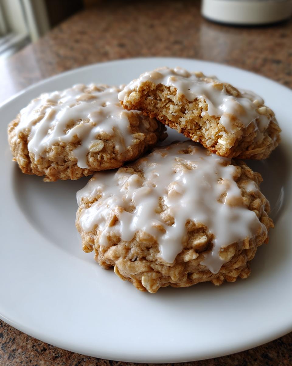 Three delicious iced oatmeal cookies stacked on a white plate, one cookie is broken open showing the texture.