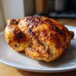 A beautifully roasted whole chicken with golden-brown, crispy skin resting on a white plate.
