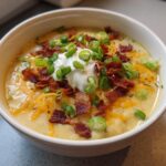 A close-up of a bowl of creamy loaded baked potato soup topped with sour cream, bacon, cheese, and green onions.