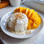 A serving of mango sticky rice featuring white sticky rice topped with toasted sesame seeds next to sliced fresh mango.