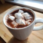 Close-up of a rich homemade hot cocoa topped with fluffy white marshmallows in a white mug.