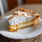 A decadent slice of butterscotch pie featuring a creamy filling, caramel layer, and tall, toasted meringue topping.