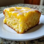 A single square of bright yellow lemon brownies topped with a white glaze, served on a white plate.