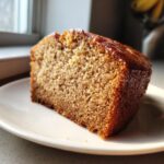 Close-up of a moist slice of banana zucchini bread on a white plate, showing its golden-brown crumb texture.
