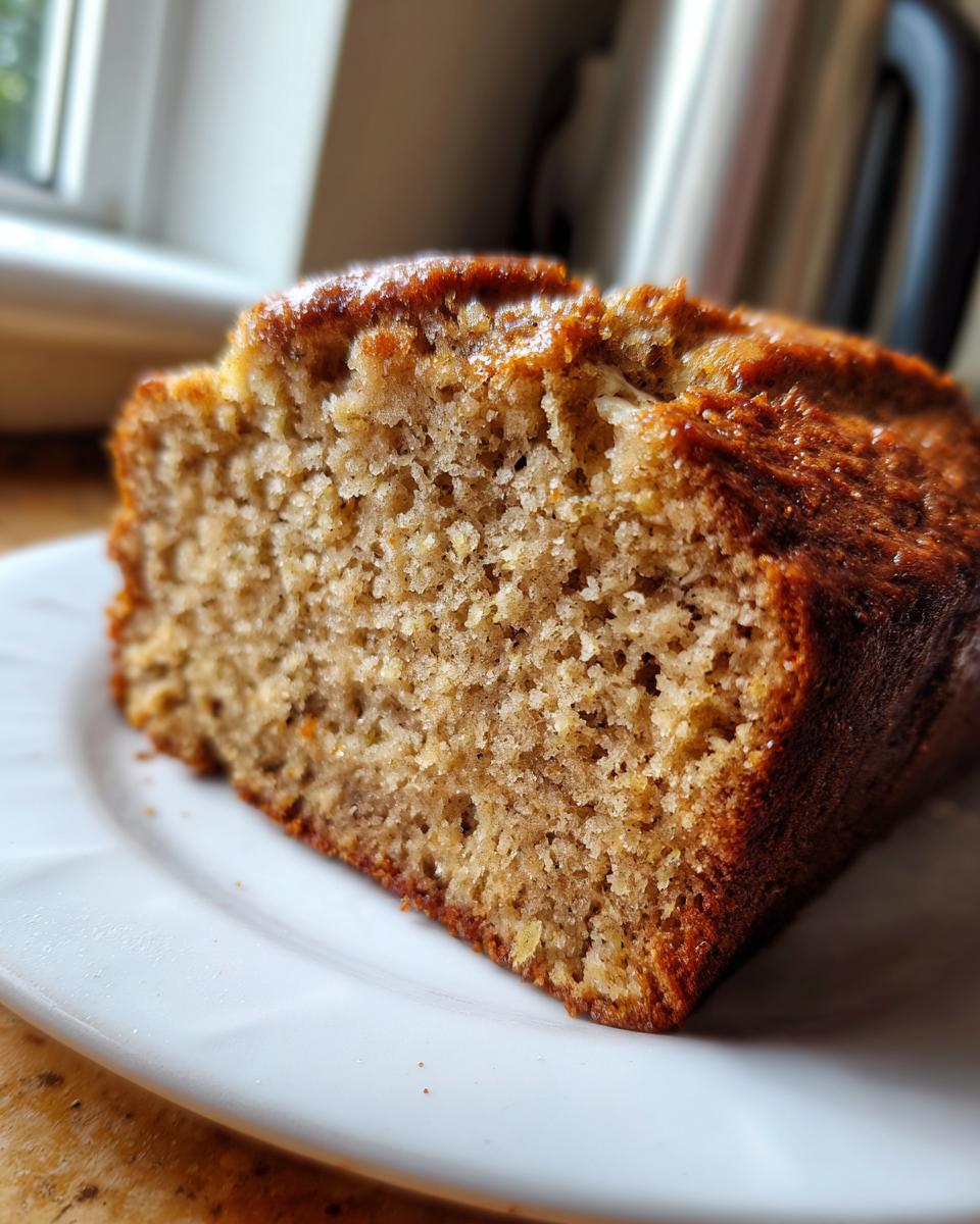 Close-up of a moist slice of banana zucchini bread with a golden-brown crust, served on a white plate.