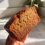 Close-up of a hand holding a thick, moist slice of golden brown vegan banana bread.