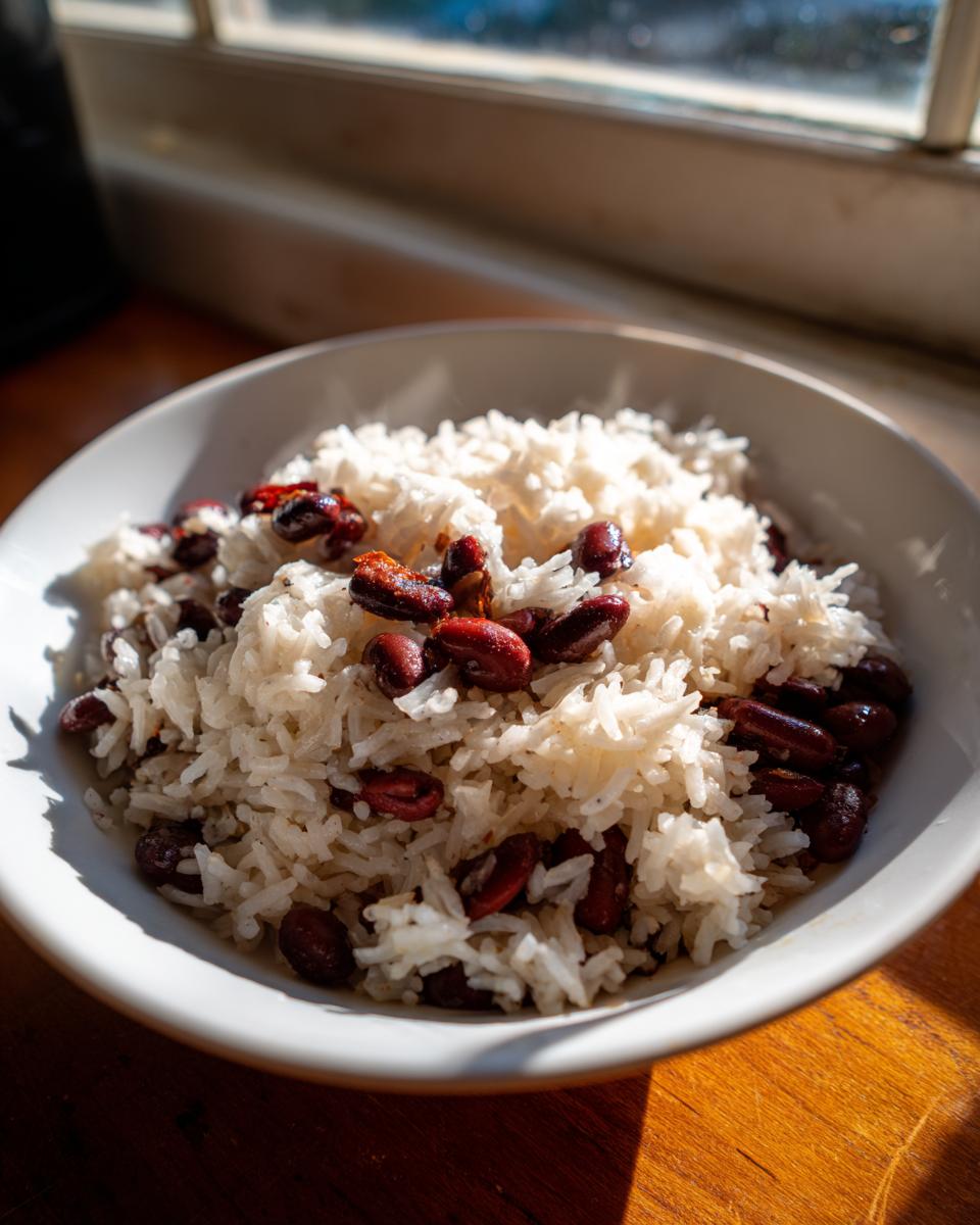 A close-up of fluffy white rice mixed with dark red kidney beans, served in a white bowl, illuminated by bright sunlight.