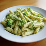 A white bowl filled with creamy penne broccoli pasta, topped with grated cheese.