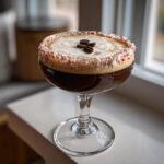 A festive peppermint espresso martini with a candy cane rim and three coffee beans on top.
