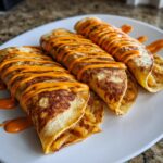 Three golden-brown potato tacos filled with seasoned potatoes and drizzled generously with bright orange sauce.