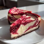 Two slices of decadent red velvet cheesecake showing a beautiful red and white swirl pattern on a white plate.