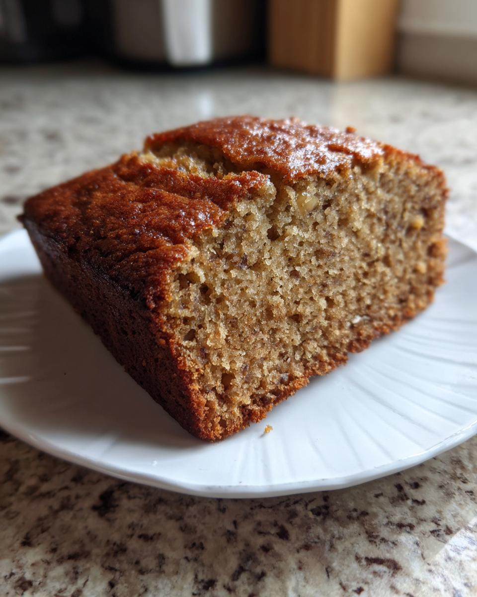 A close-up of a thick slice of moist banana bread recipe showing its rich brown crust and soft interior.