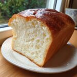 A close-up of a freshly baked loaf of condensed milk bread, showing its incredibly soft, fluffy white crumb and golden-brown crust.