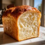 A freshly baked loaf of sourdough sandwich bread, sliced to show its incredibly soft and fluffy white interior crumb.