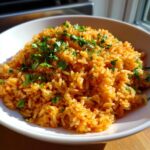 Close-up of a white bowl filled with vibrant orange Spanish rice, garnished generously with fresh chopped cilantro.
