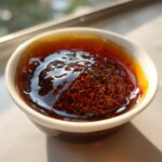 Close-up of thick, glossy, dark brown teriyaki sauce with a honeycomb-like bubble pattern, held in a small white dipping bowl.
