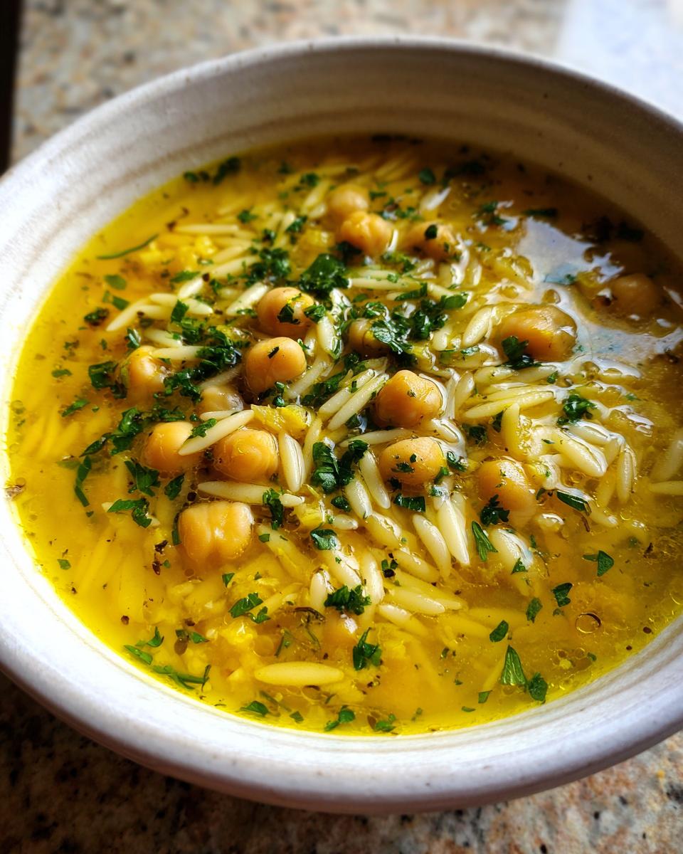 Close-up of a bowl of vibrant yellow chickpea soup featuring orzo pasta, whole chickpeas, and fresh parsley.