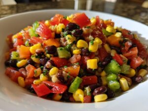 Close-up of a white bowl filled with colorful cowboy caviar, featuring black beans, corn, tomatoes, and peppers.