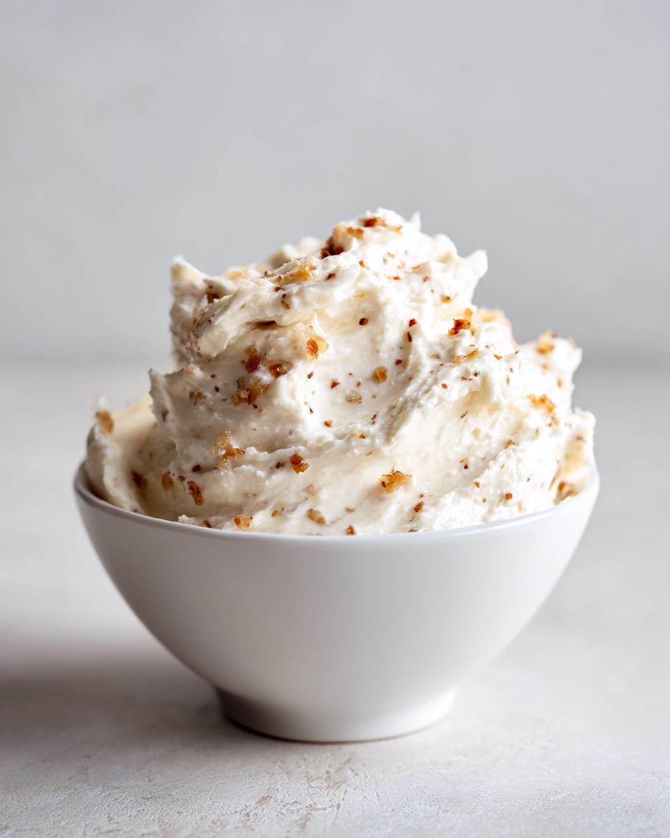 A creamy mound of caramelized onion dip, speckled with brown onion bits, served in a small white bowl.