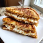 Two halves of golden brown apple cinnamon cream cheese stuffed french toast stacked on a white plate.