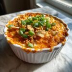 Close-up of baked chili cream cheese dip topped with crushed chips and green onions.
