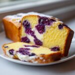 A close-up of a sliced blueberry cream cheese bread loaf showing the yellow cake, purple blueberries, and white cream cheese swirl.
