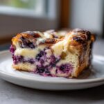 A close-up of a rich slice of blueberry cream cheese bread pudding with a golden-brown top.