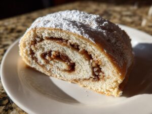 Cross-section view of a buttery Italian nut roll cookie filled with dark nut paste and topped with powdered sugar.