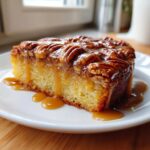 Close-up of a moist slice of caramel pecan upside down cake generously drizzled with warm caramel sauce.
