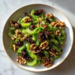 A close-up overhead view of a vibrant celery salad with walnuts and dates in a light bowl.