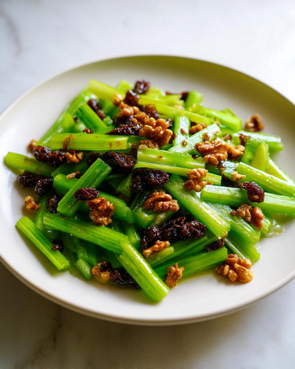 A vibrant plate of celery salad with walnuts and dates, featuring bright green celery sticks mixed with dark raisins and crunchy walnuts.